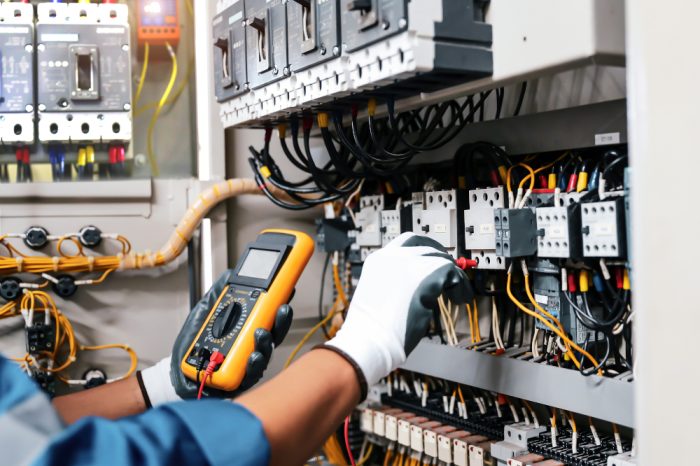 Electricity or electrical maintenance service, Electrician hand holding measuring meter checking electric current voltage circuit breaker cable wiring check main power load center distribution board.